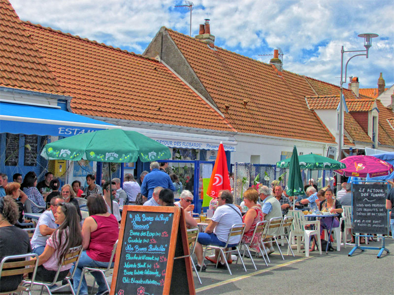 People enjoying plates of sea food at a terraced restaurant on a sunny day, colourful umbrellas give shade