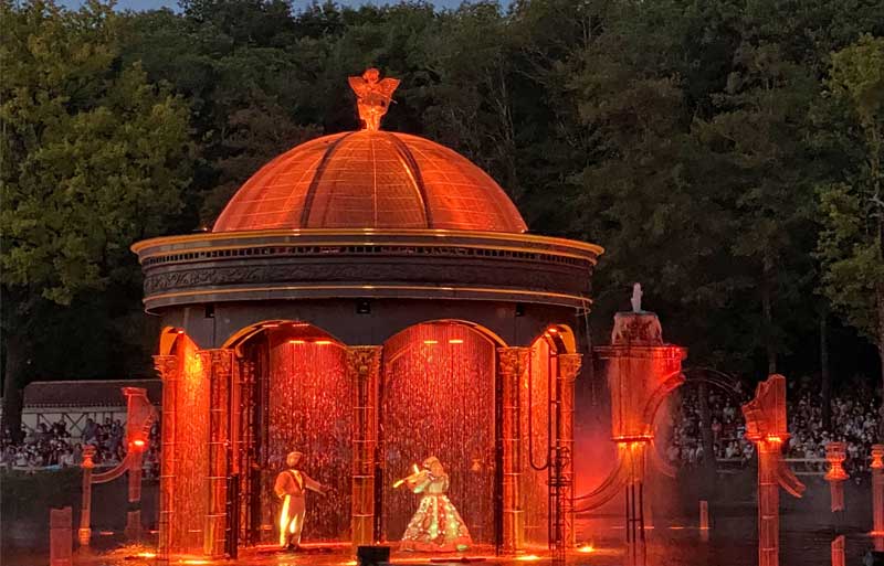 A pavillion in a lake, lit up as a dancer plays a violin at the Puy du Fou theme park